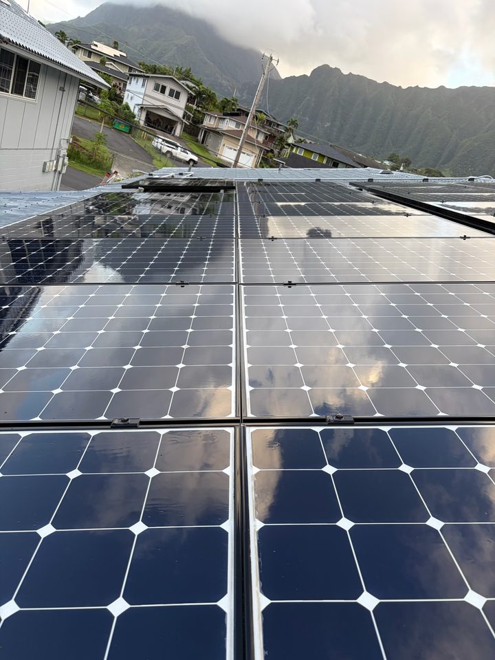 Clean solar panels reflecting the clouds, with the mountains behind