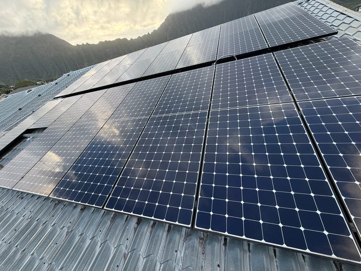 A full array of clean solar panels on a metal tile roof below green mountain ridges