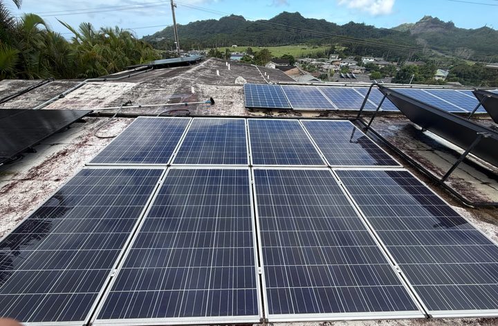 A grid of clean solar panels on a flat roof, with the ridge line in the distance