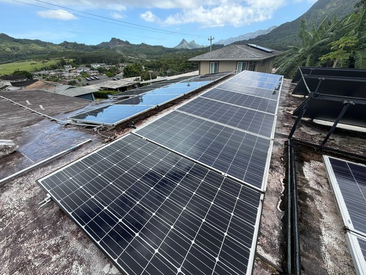 Rows of solar panels on a flat roof with green mountains and blue sky behind