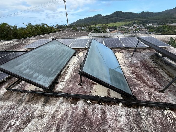 Two solar water heater collectors with clean glass on a flat roof, mountains behind