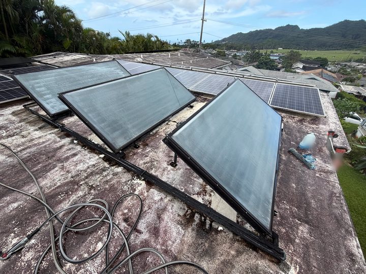 Three solar water heater collector panels tilted up on racks on a flat roof